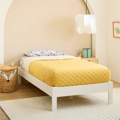 a bed with yellow bedspread in a bedroom next to a white dresser and lamp