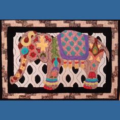 an elephant made out of fabric on a wall hanging from a blue frame with black border