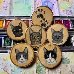 four wood slices with pictures of cats on them in front of paintbrushes and watercolors