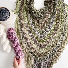 a person holding yarn next to a crocheted shawl