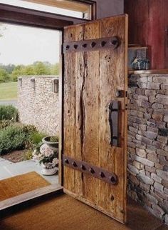 an open wooden door in front of a brick wall and stone fireplace with potted plants next to it