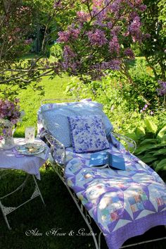 a lawn chair with a quilt on it next to a table and flowers in the background