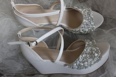 two pairs of white shoes with pearls on the top and bottom, sitting on a bed