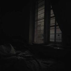 a dark room with an unmade bed and window