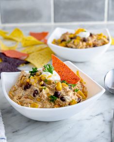 two white bowls filled with food on top of a marble counter next to tortilla chips