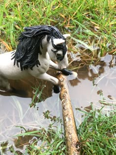 a toy horse that is standing in the water with a stick on it's back