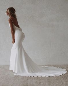 a woman in a white wedding dress is standing against a wall with her back to the camera