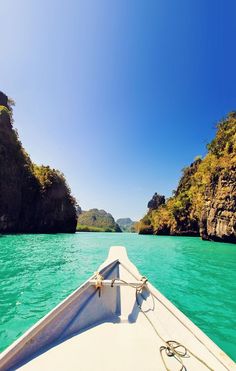 the bow of a boat traveling through clear blue water with cliffs in the back ground