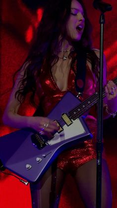 a woman in a red dress is holding a blue guitar and singing into a microphone