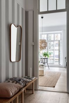 the hallway is decorated with striped walls and wood flooring, along with a bench that has pillows on it