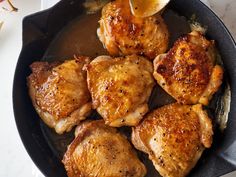 some chicken is cooking in a pan on the stove top and being served with lemon wedges