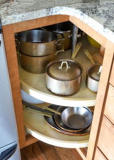 pots and pans are sitting in the corner of a kitchen cabinet with wooden shelves