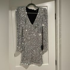 a silver sequin dress hanging on a white door with a black shirt underneath it