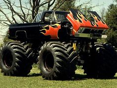 a monster truck with flames painted on it's front and rear tires is parked in the grass