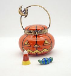 an orange pumpkin shaped tea pot next to two small candy cornucons on a white surface