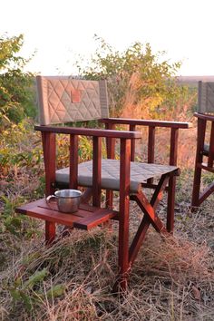 two wooden chairs sitting on top of a dry grass covered field next to each other