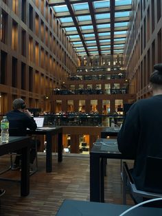 two people are sitting at tables in an office building, one is on his laptop