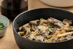 a bowl filled with pasta and meat next to a glass of wine on a table