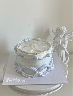 a white cake sitting on top of a table next to an angel figurine