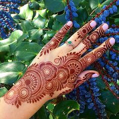 a woman's hand with henna on it and blue berries in the background