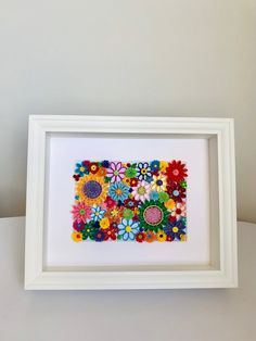 a white frame with colorful flowers in it on top of a table next to a wall