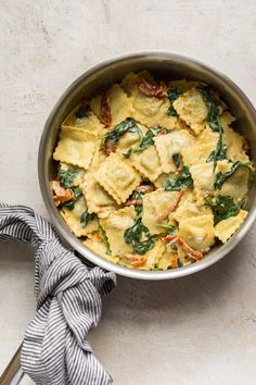 a pan filled with pasta and spinach on top of a table next to a napkin