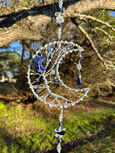 a wind chime hanging from a tree branch with beads and crystals in the shape of a crescent