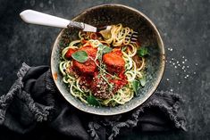 a bowl filled with spaghetti and meatballs on top of a black cloth next to a fork