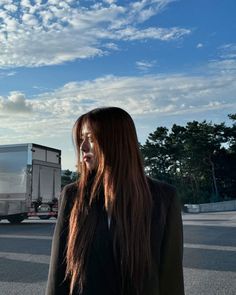 a woman with long hair standing in the middle of an empty parking lot next to a truck