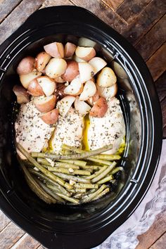 chicken, potatoes and asparagus in the crock pot on top of a wooden table