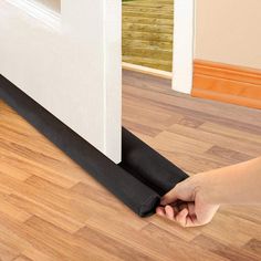 a hand is holding the edge of a black mat near a white wall and wooden floor