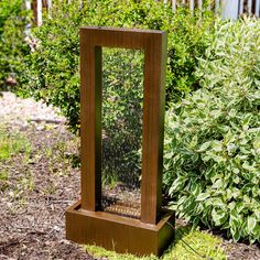 a bird cage sitting on top of a wooden stand in front of some bushes and shrubbery