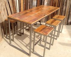 a wooden table sitting next to two metal stools on top of a cement floor