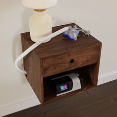 a wooden night stand with an electric hair dryer on it and a lamp next to it