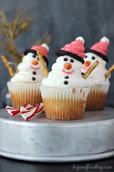 three cupcakes with frosting and candy canes in the shape of snowmen