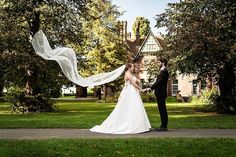 a bride and groom standing in front of a house with their veil blowing in the wind