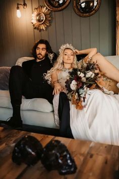 a man and woman sitting on a couch with flowers in their hair posing for a photo