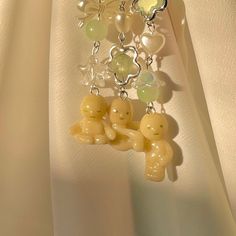 a pair of earrings with charms attached to them on a white fabric background and some beads hanging from it