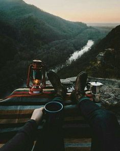 a person sitting on top of a blanket next to a coffee cup and an lantern