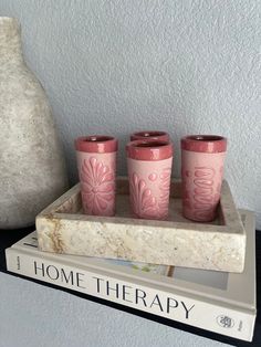 three pink glasses sitting on top of a marble tray next to a vase and book