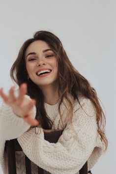 a smiling woman sitting in a chair with her hands out and looking up at the camera