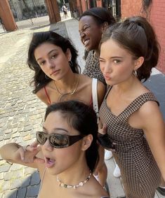 three women standing next to each other in front of a brick wall and one has her tongue out