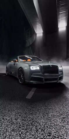 the front end of a grey sports car parked under a bridge at night with fog in the air