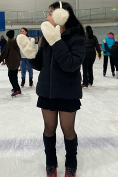 a woman is standing on an ice rink with her hands up to her face while wearing gloves