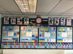 a bulletin board with lots of pictures on it in a school classroom area, and a clock hanging from the ceiling