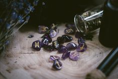 amethyst stones are scattered on a wooden surface next to a glass bottle and flowers