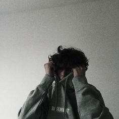 a man in grey hoodie holding his head to his ear while looking up at the ceiling