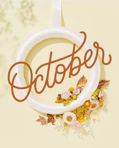 a white circle with the word october hanging from it's center surrounded by flowers