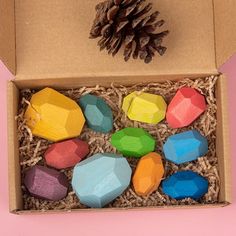 a box filled with wooden toys next to a pine cone on top of a pink surface