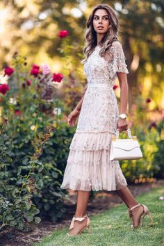 a woman in a dress and heels is walking through the grass with flowers behind her